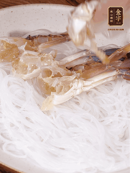 盤底墊上粉絲，擺上梭子蟹、火腿片，撒姜粒，淋上蒸魚豉油、花雕酒調(diào)味腌制15分鐘